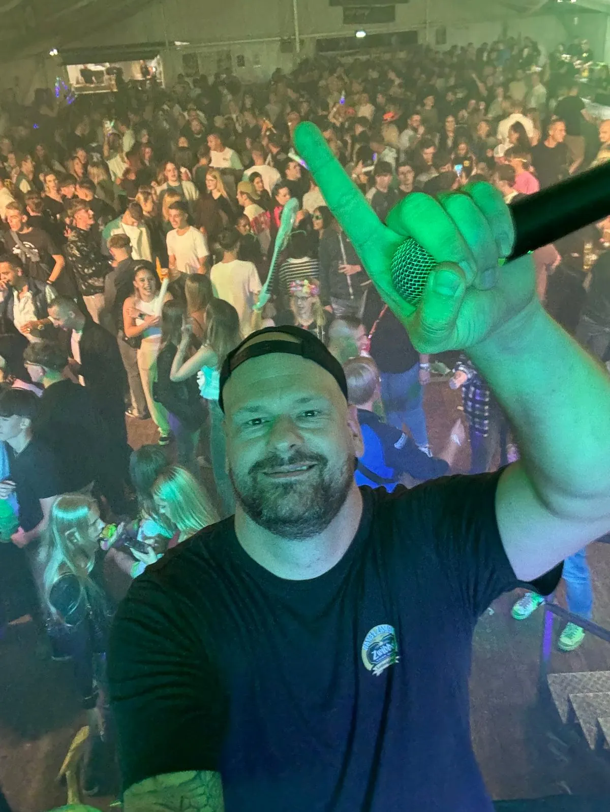 Marian am DJ-Pult vor einem vollen Festzelt, die Menge tanzt im grünen Bühnenlicht